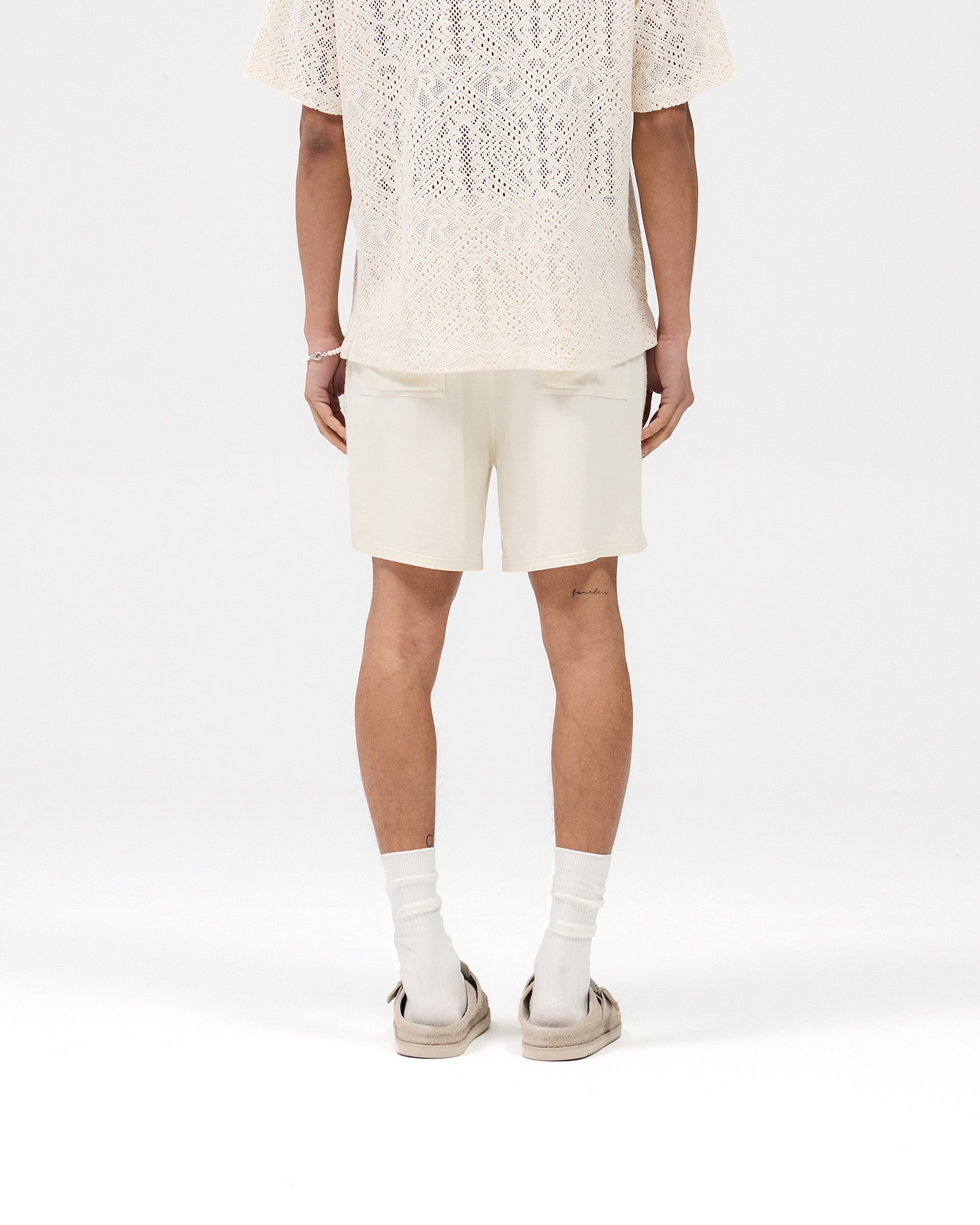 Man wearing white shorts on a plain white background | Knitted Panel Short in Antique White | Shorts with elasticated waistband and knitted panel detailing | SS25 Shorts | Represent Clo
