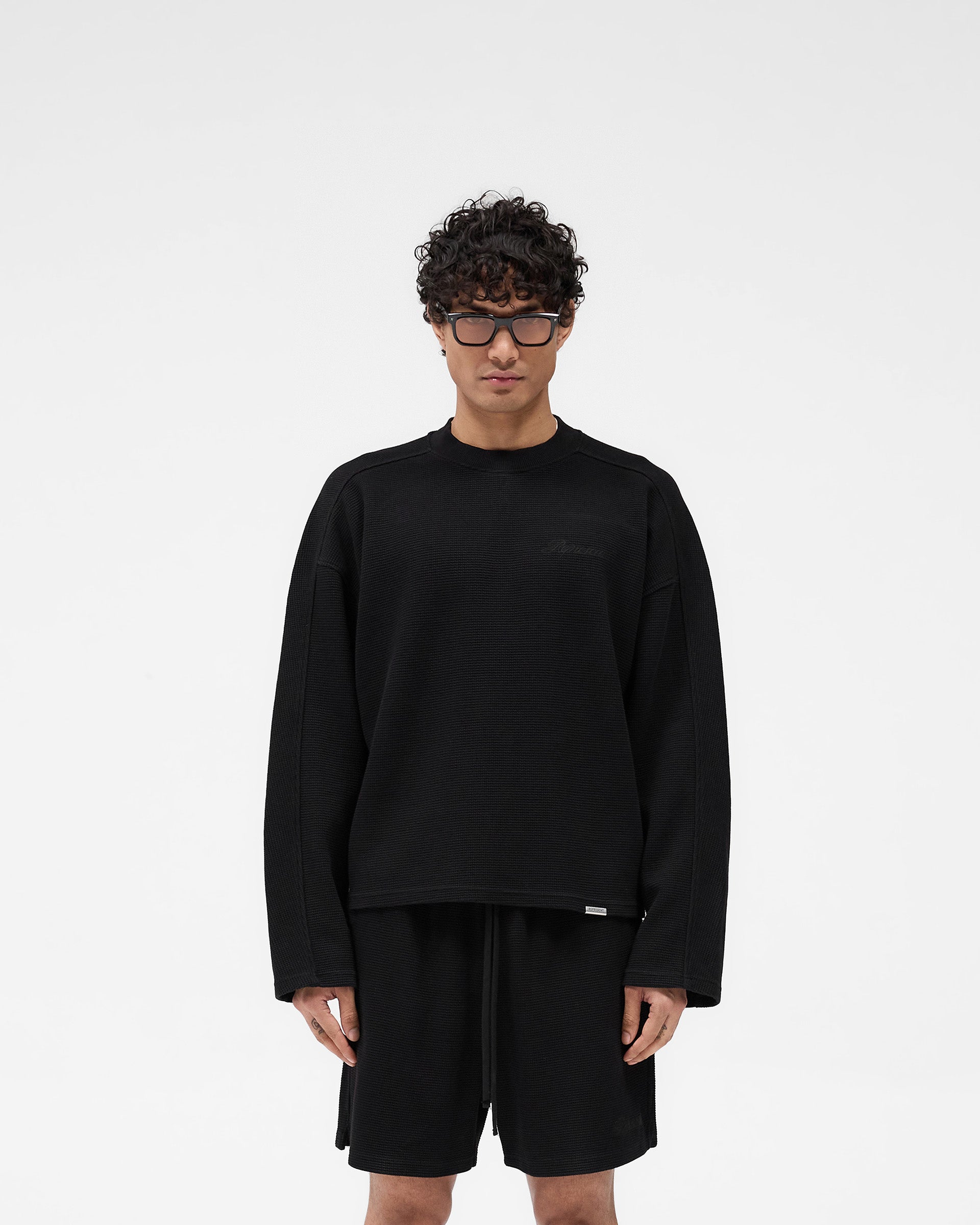 Man wearing a black long sleeve t-shirt on a plain white background | Waffle Long Sleeve T-Shirt in Black | Textured waffle fabric long sleeve T-shirt with boxy fit | SS25 T-Shirts | Represent Clo