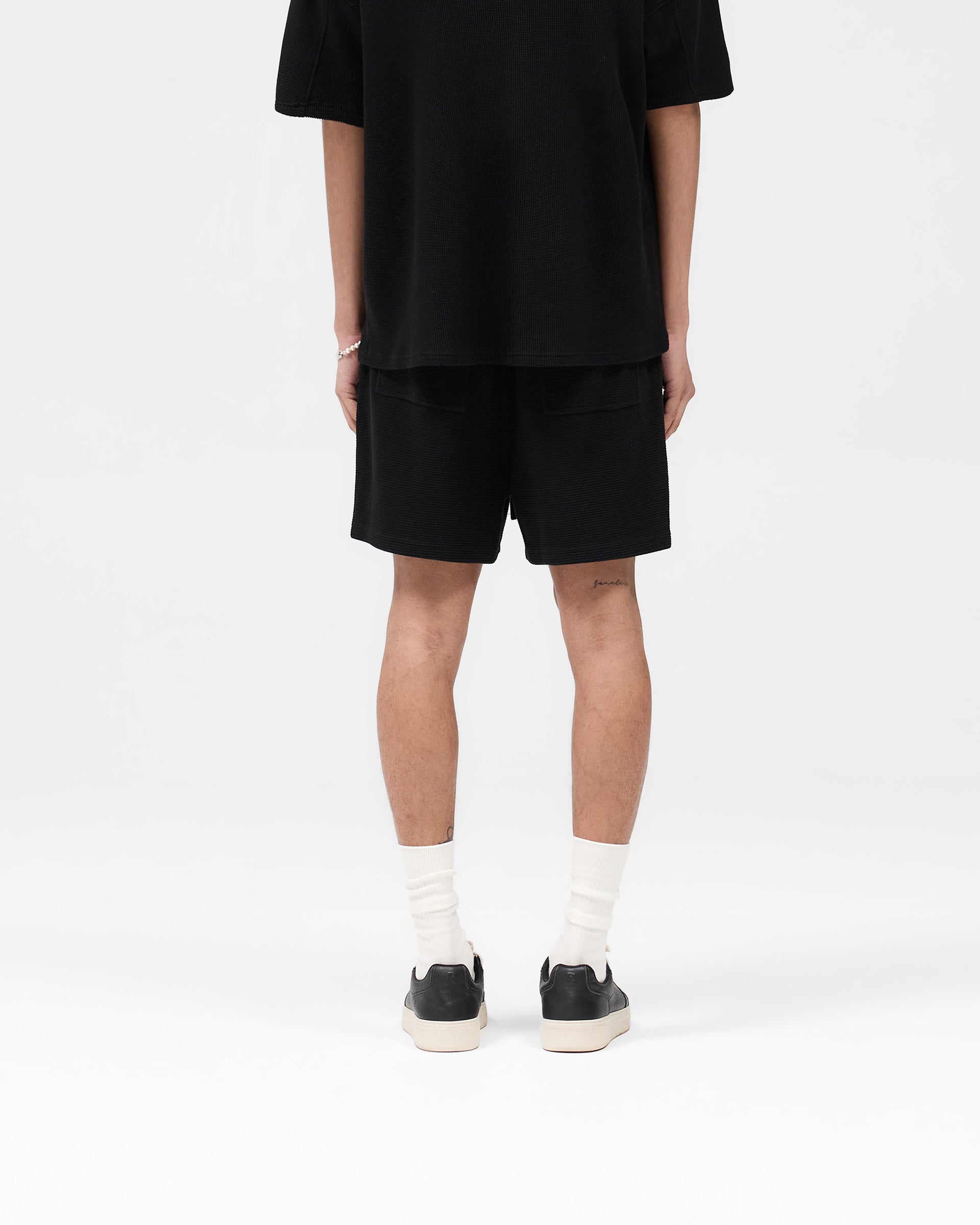 Man wearing black waffle shorts on a plain white background | Waffle Shorts in Black | Heavyweight waffle fabric shorts with elasticated waistband | SS25 Shorts | Represent Clo
