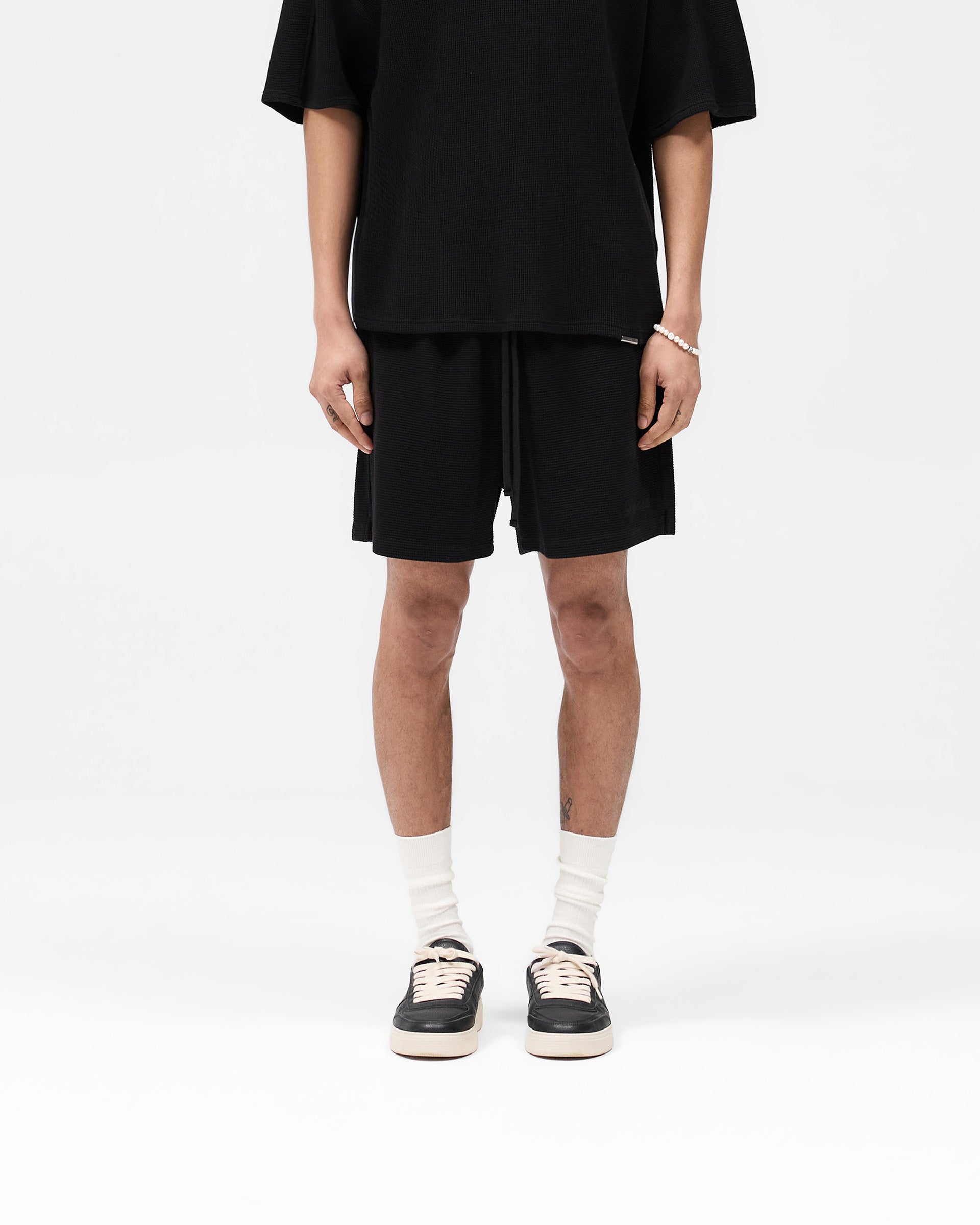 Man wearing black waffle shorts on a plain white background | Waffle Shorts in Black | Heavyweight waffle fabric shorts with elasticated waistband | SS25 Shorts | Represent Clo
