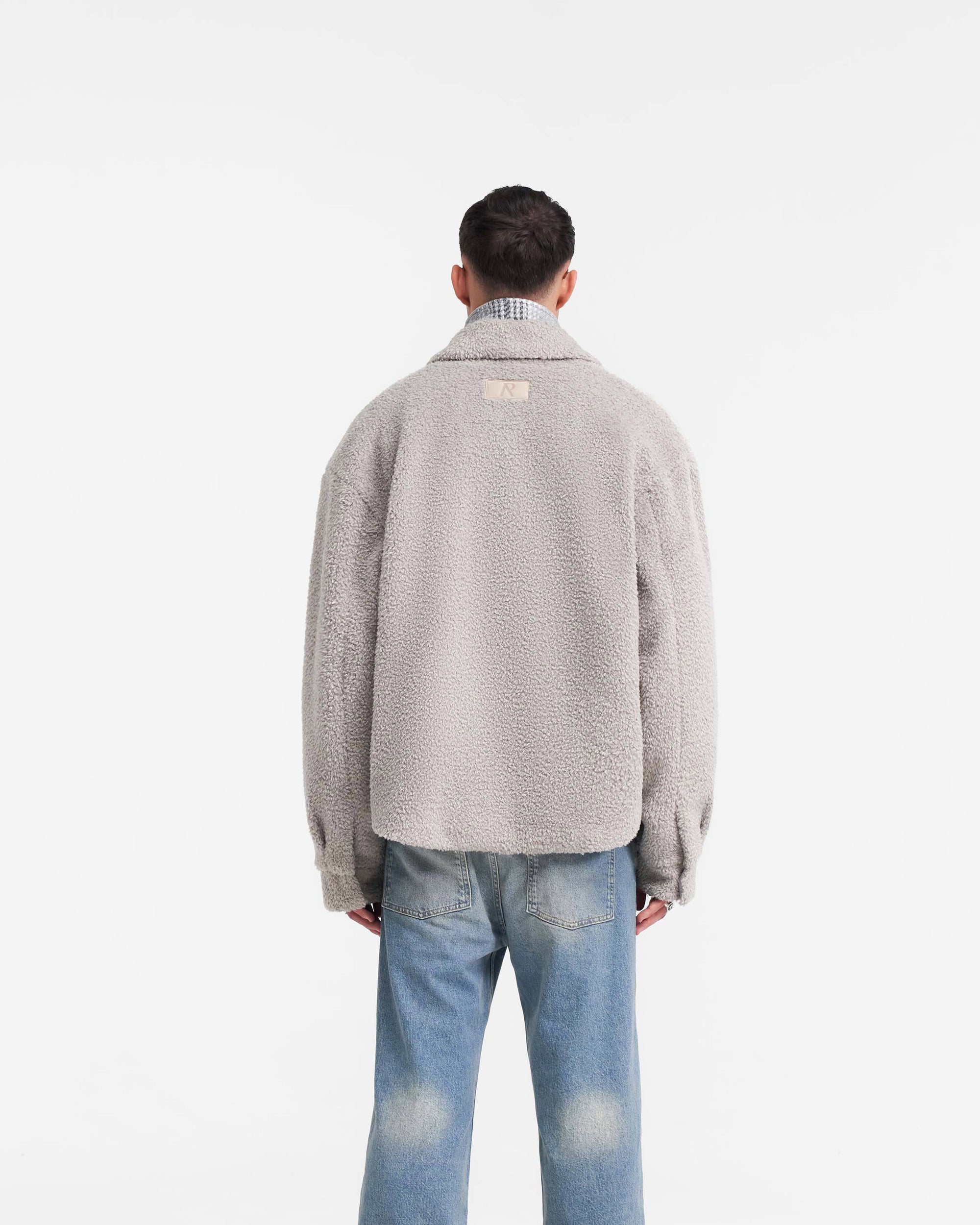Man wearing a grey shearling shirt on a plain white background | Shearling Scoop Hem Shirt in Ice Grey | Shearling shirt with zip and popper closure | PRE SS24 Shirts | Represent Clo