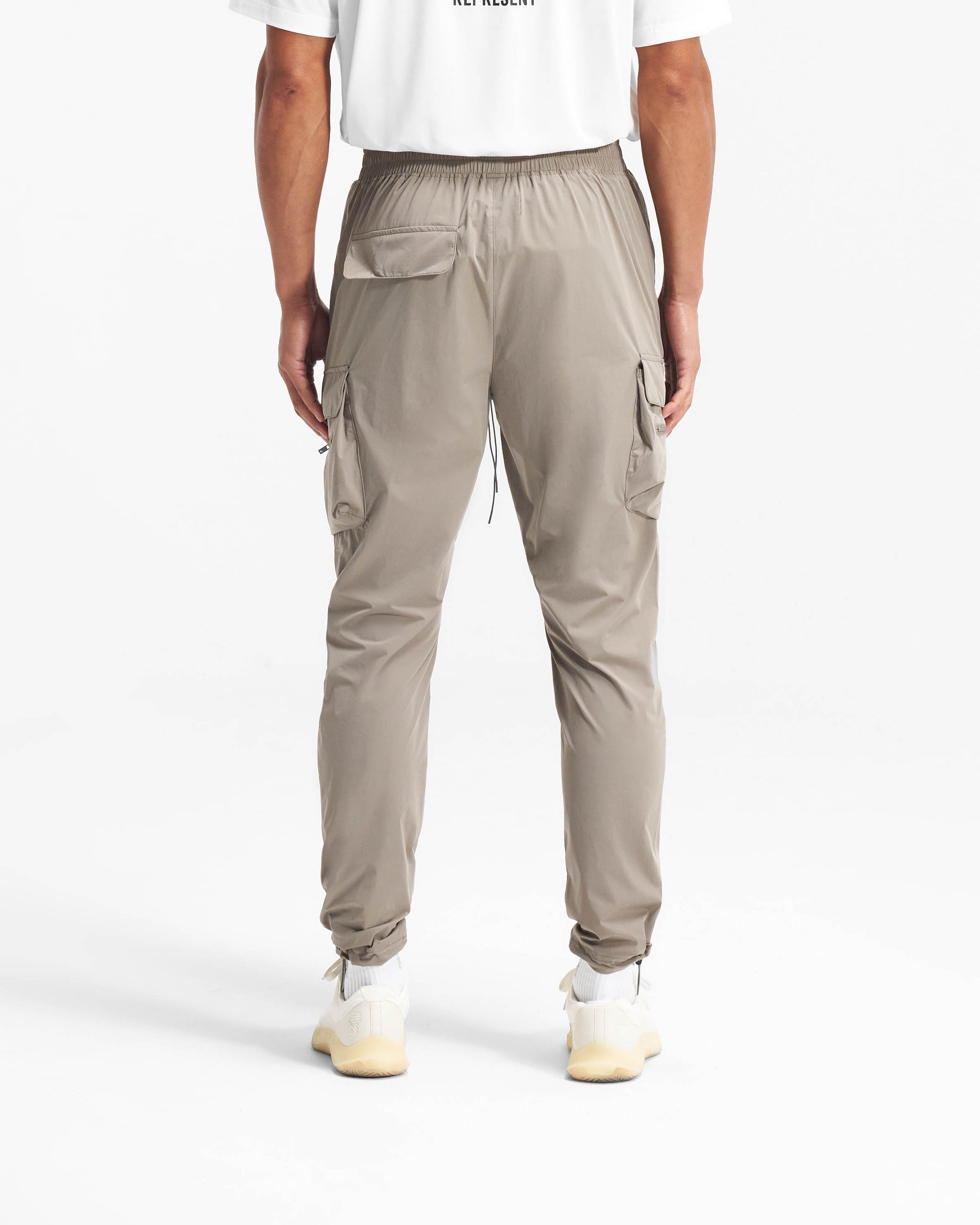 Man wearing taupe cargo pants on a plain white background | 247 Pant in Taupe | Cargo pants with elasticated waistband and zip side pockets | 247 Pants | Represent Clo