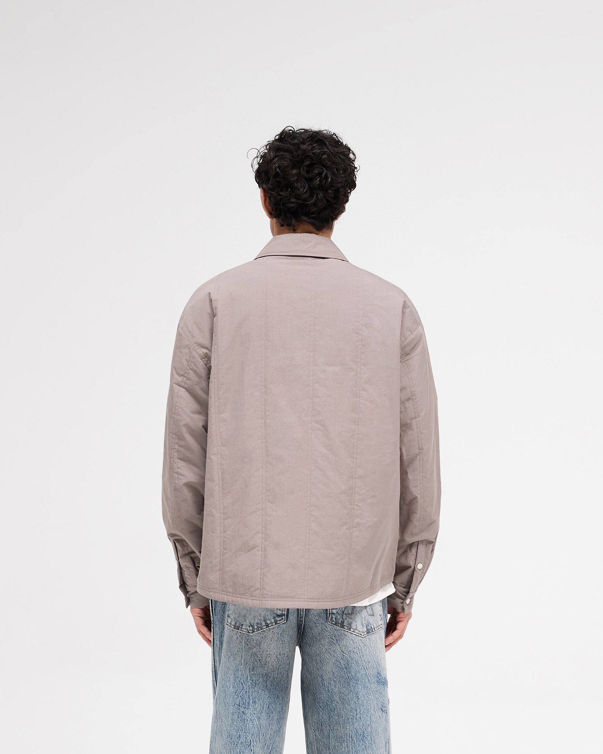 Man wearing a grey quilted overshirt on a plain white background | Quilted Overshirt in Mid Grey | Shirts with twin needle quilting stitches and chest pockets | SS25 Shirts | Represent Clo