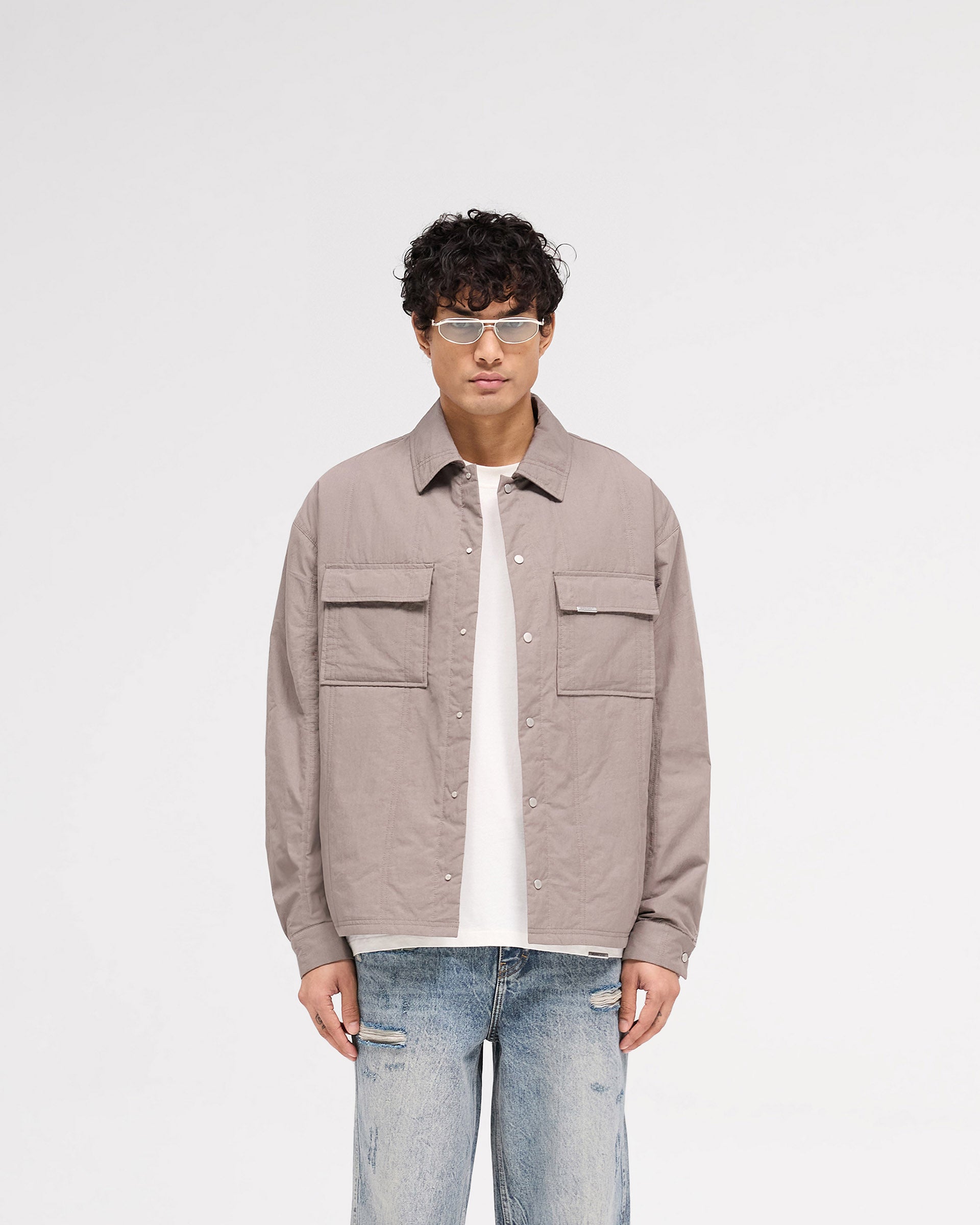 Man wearing a grey quilted overshirt on a plain white background | Quilted Overshirt in Mid Grey | Quilted shirt with light wadding and chest pockets | SS25 Shirts | Represent Clo