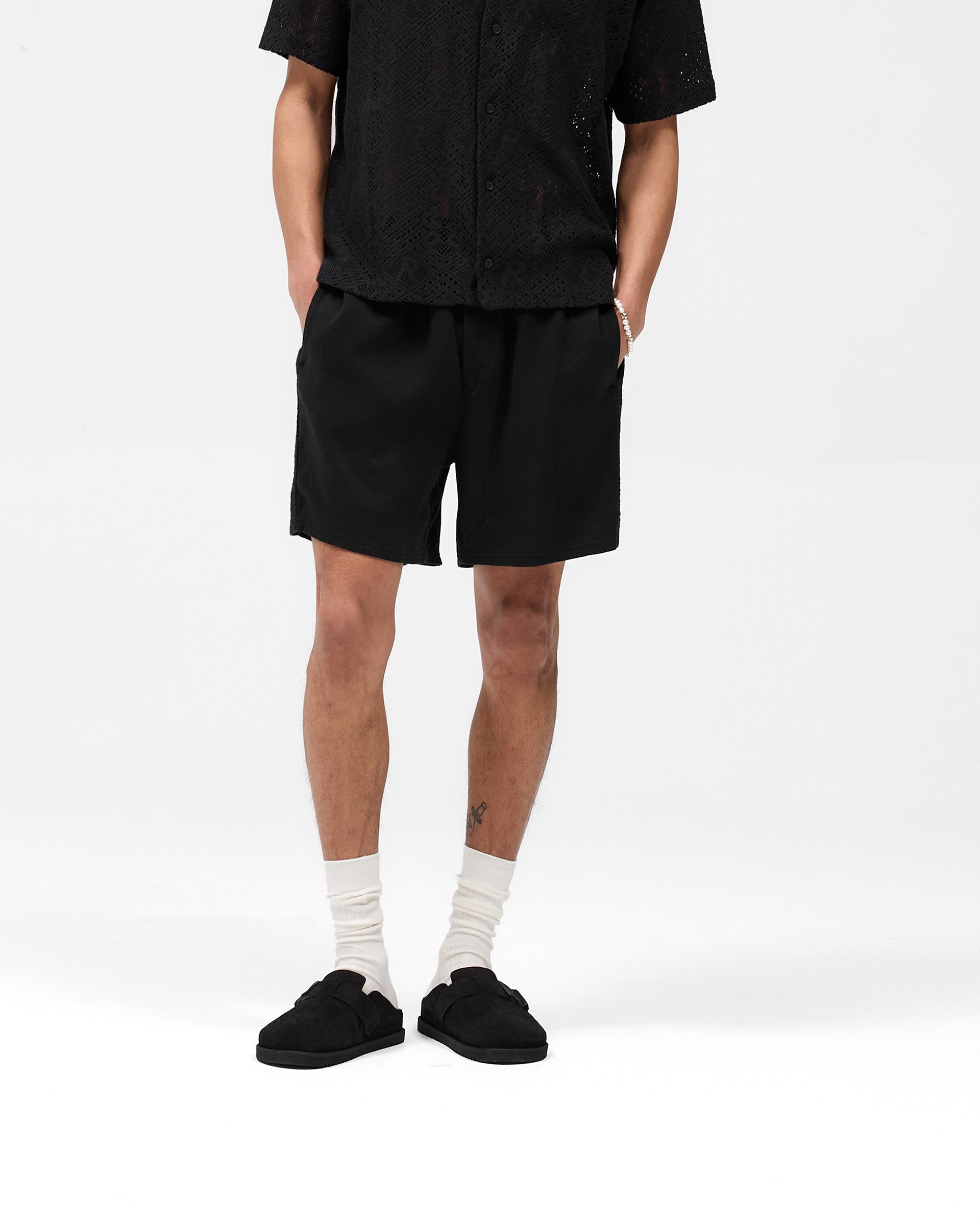 Man wearing black shorts with knitted side panels on a plain white background | Knitted Panel Short in Black | Shorts with elasticated waistband and slip pockets | SS25 Shorts | Represent Clo