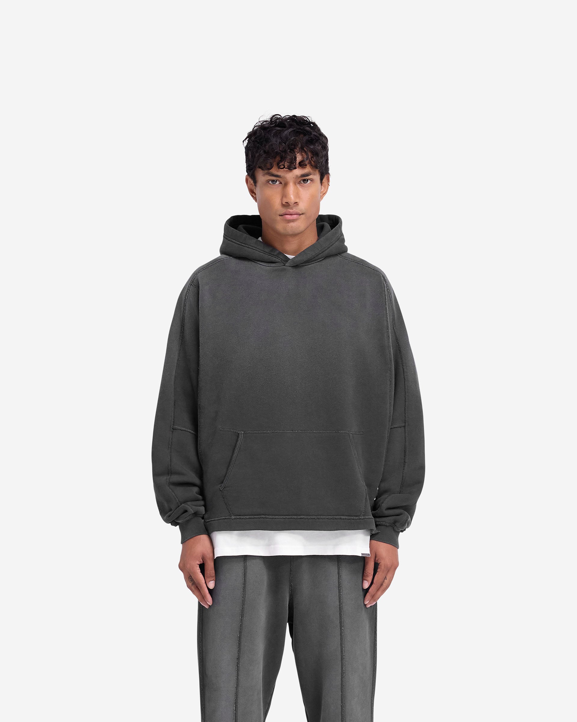 Man wearing an oversized black hoodie on a plain white background | Stepped Hem Hoodie in Stained Black | Split stepped hem and raw edge patch | FW24 Hoodies | Represent Clo