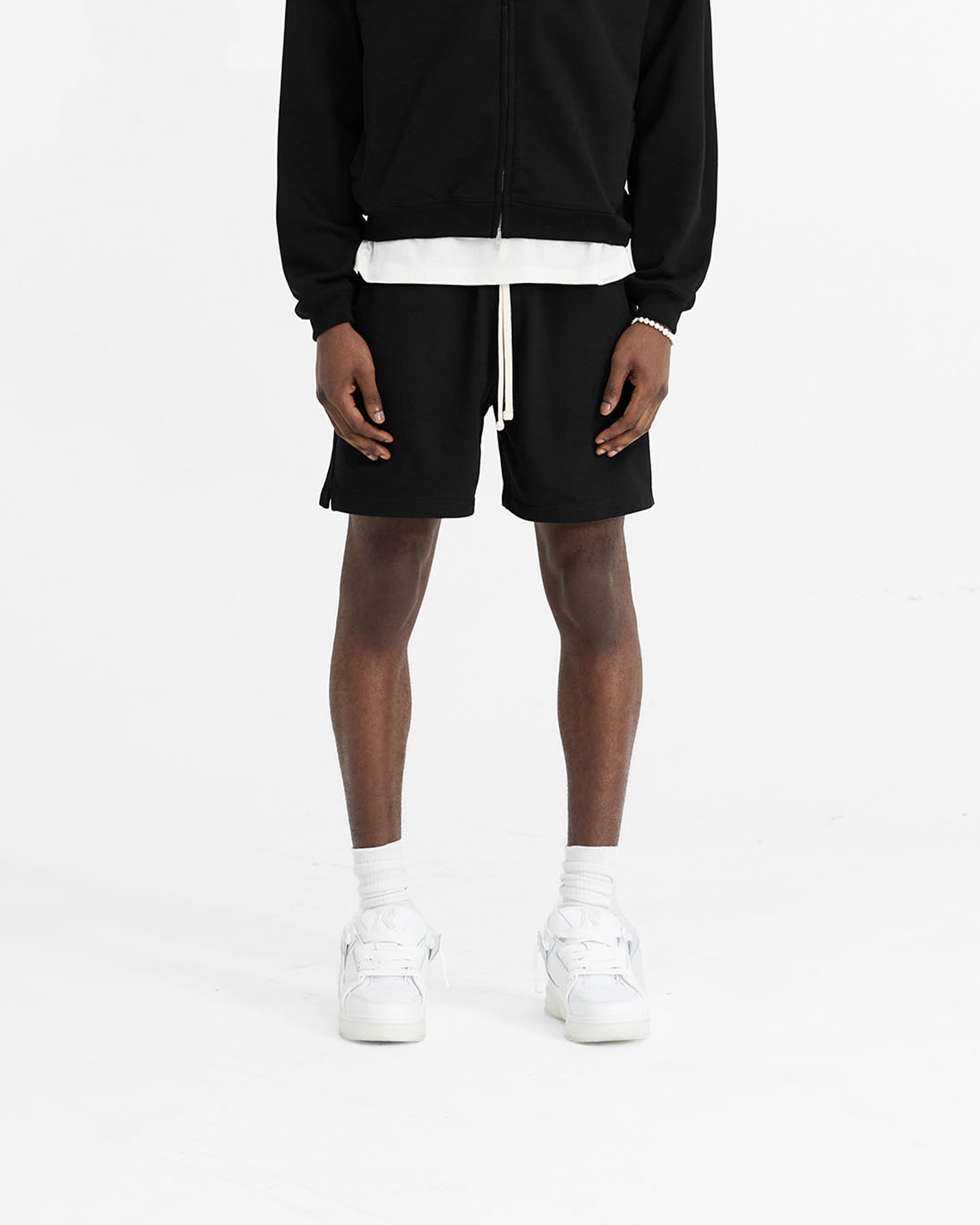 Man wearing black sweatshorts on a plain white background | Initial Sweatshorts in Black | Oversized boxy fit sweatshorts with elasticated waistband | Initial Shorts | Represent Clo